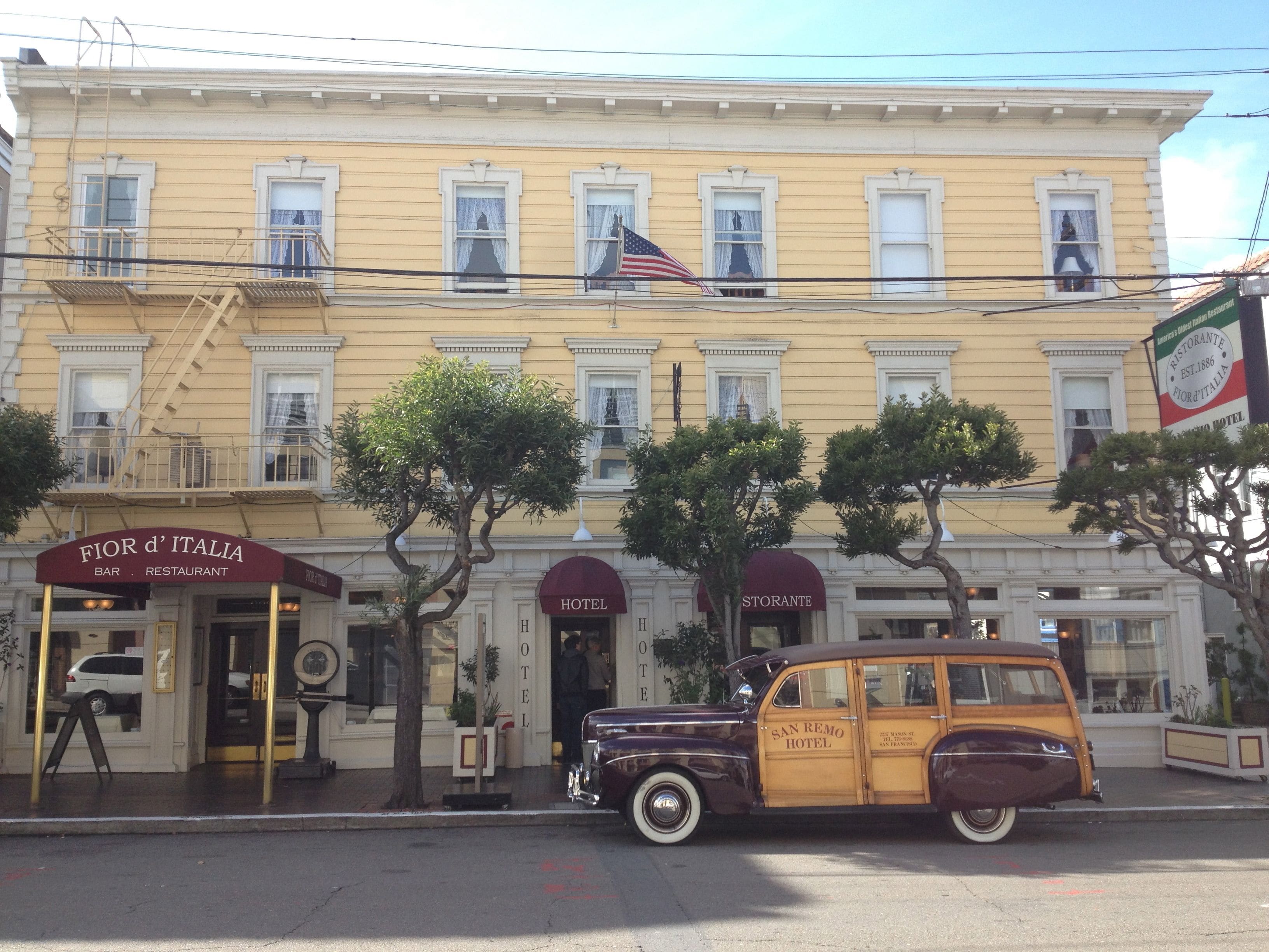 A historic building with a yellow facade, multiple windows, and a vintage car parked in front.