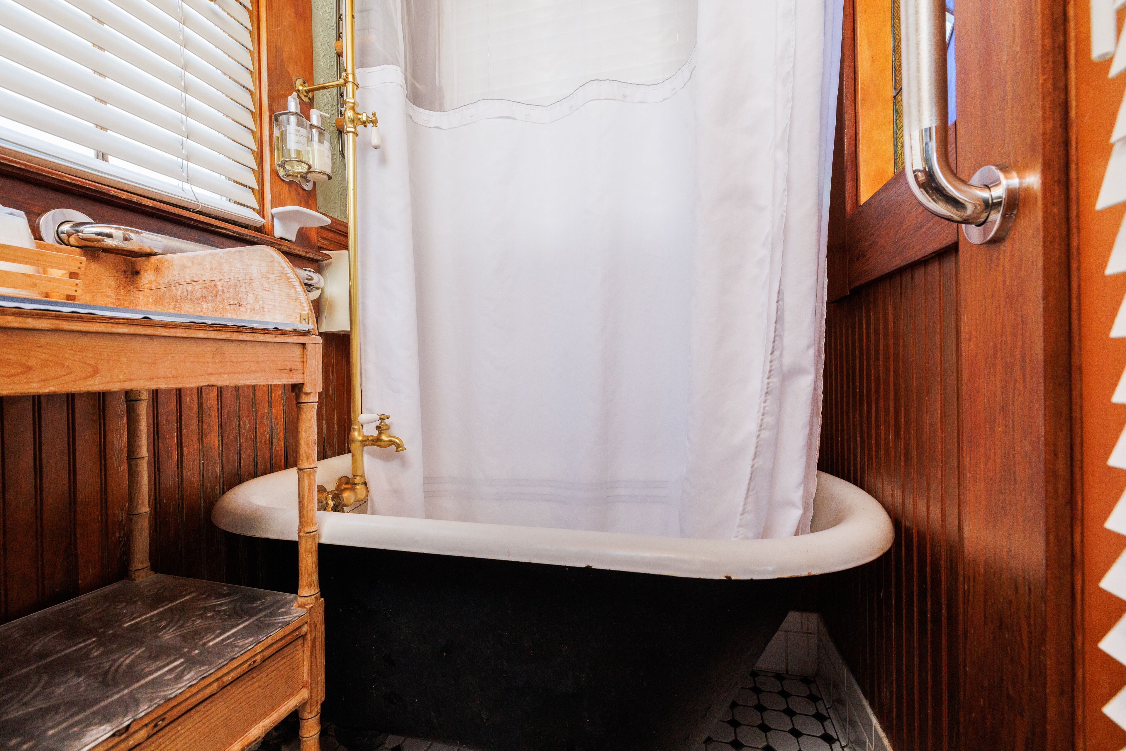 A vintage bathroom with a clawfoot bathtub, wooden paneling, a wooden bench, and a white sink.