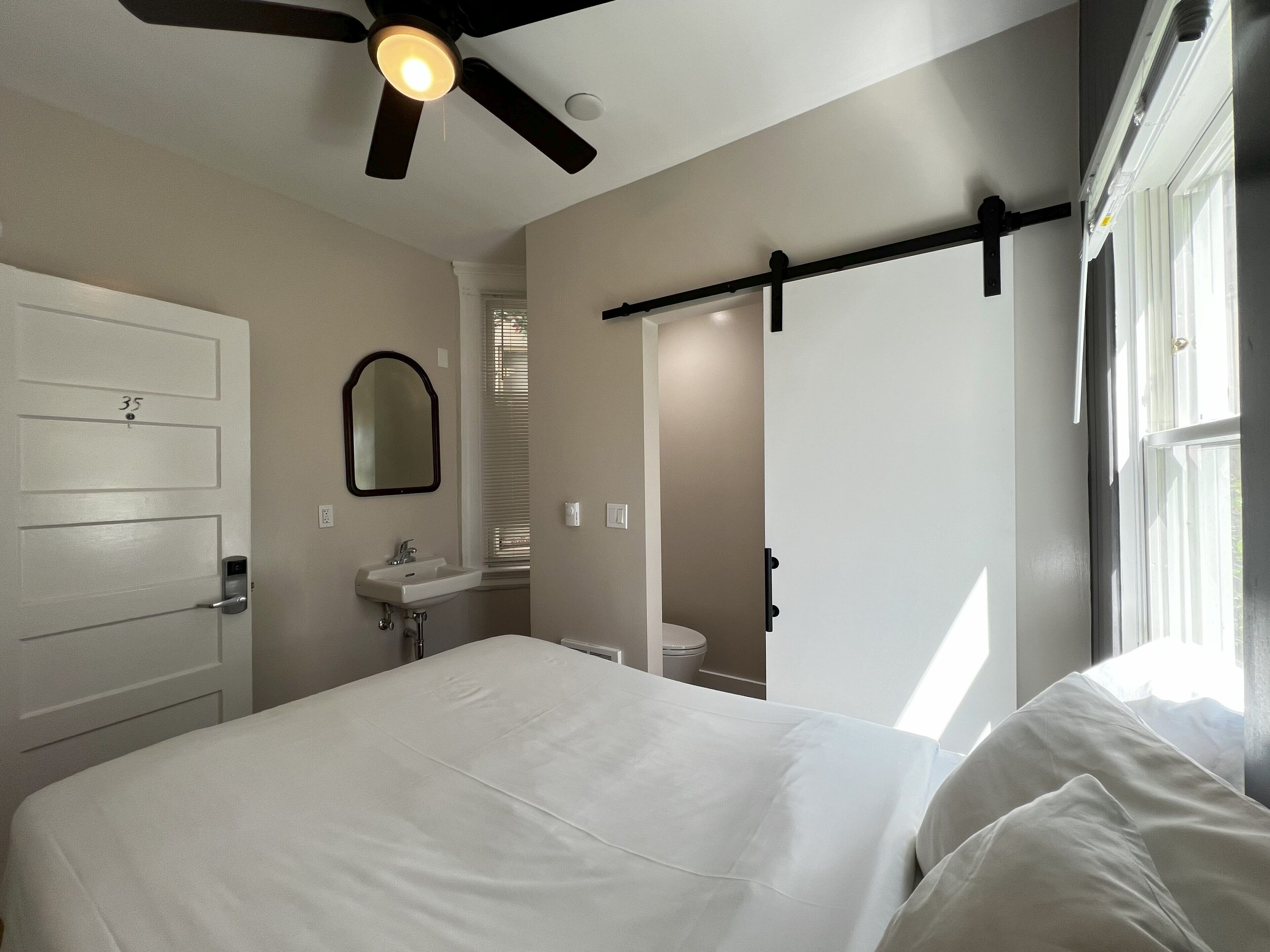 Un dormitorio con cama, ventilador de techo, ventana y puerta con un número.