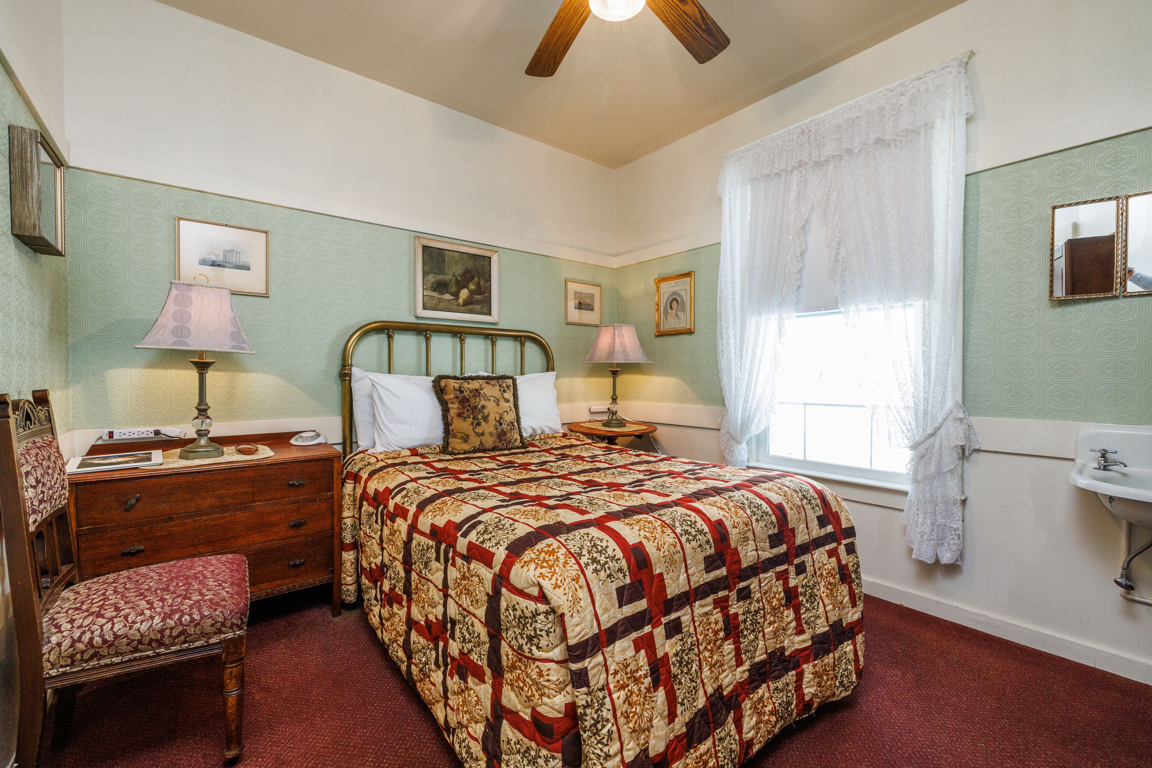 A bedroom with a bed, dresser, chair, bedside tables, and a window with curtains.