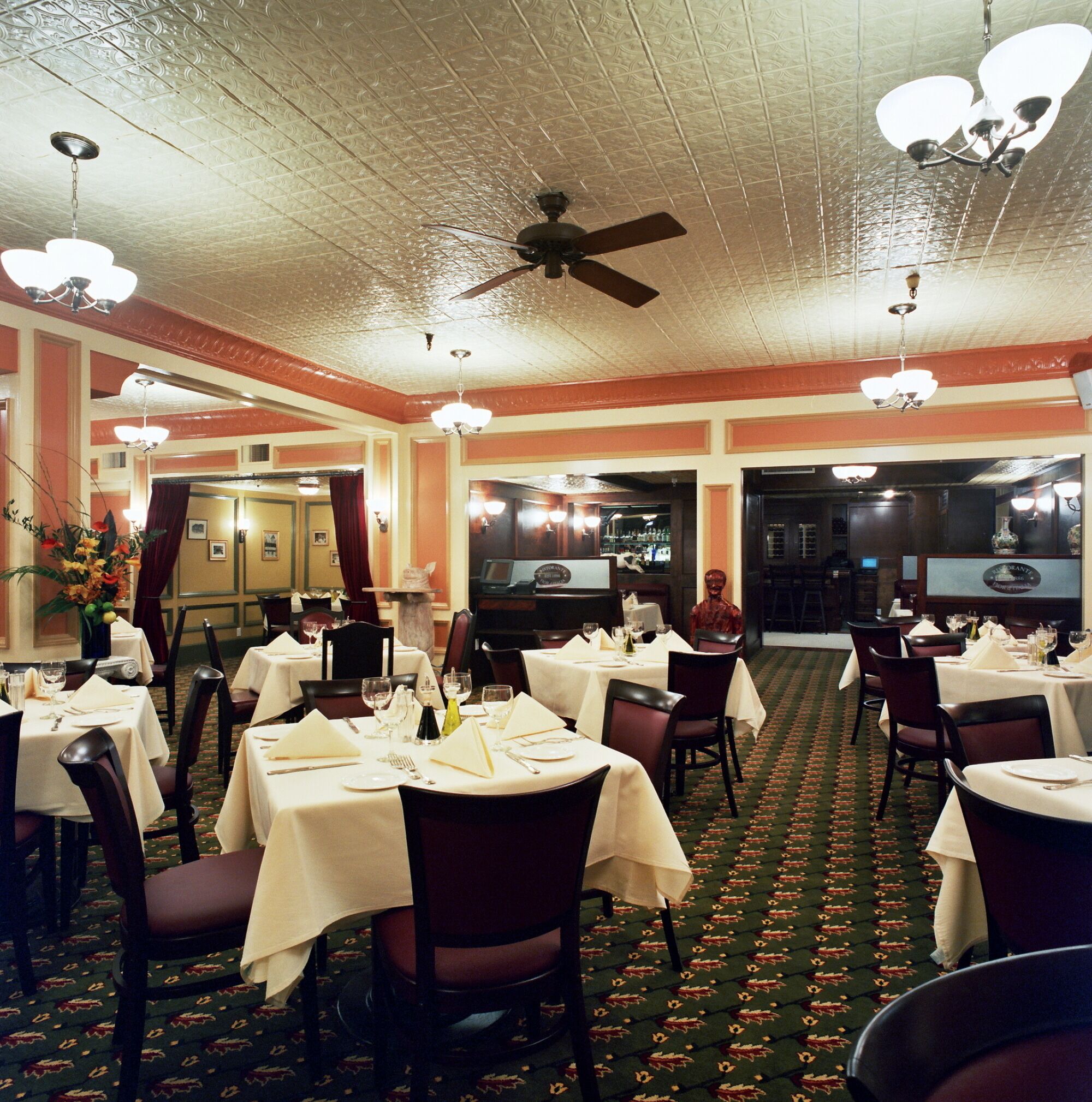 A restaurant with multiple tables set for dining, a ceiling fan, and a bar area in the background.