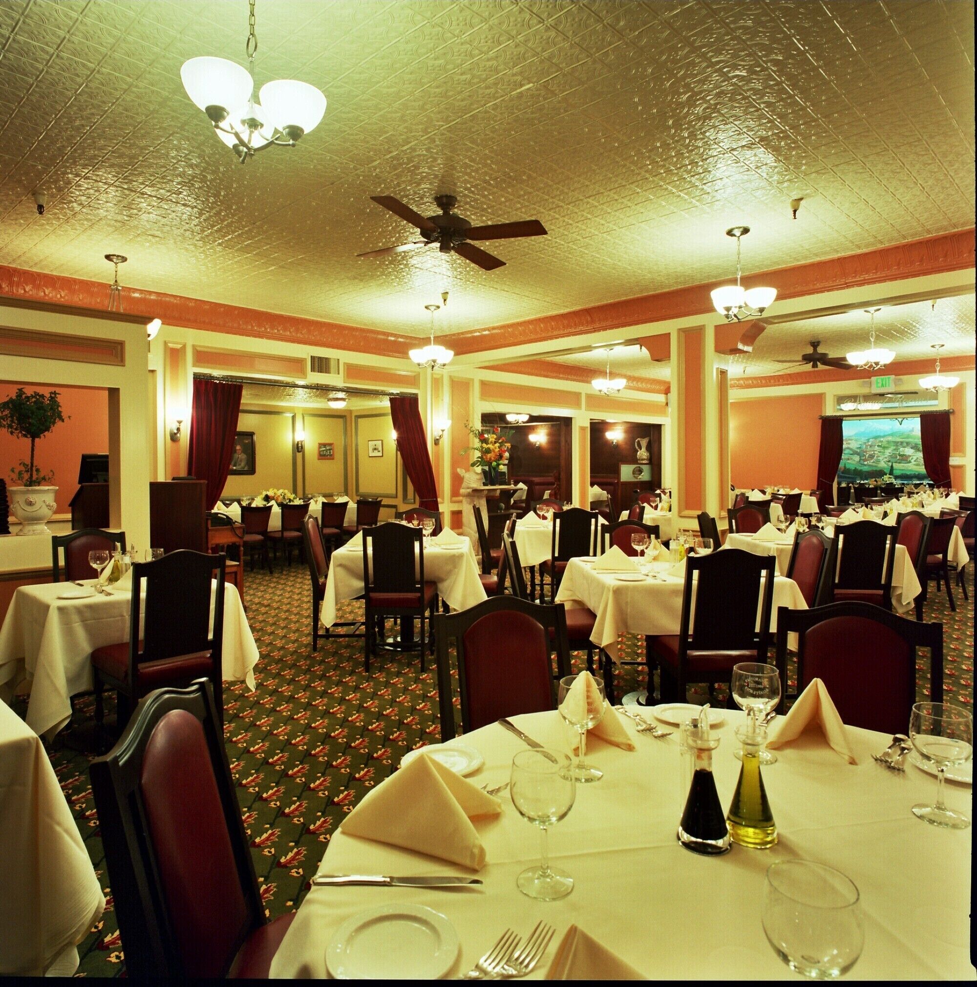 Un restaurante con varias mesas dispuestas para comer, ventiladores de techo y una televisión grande al fondo.
