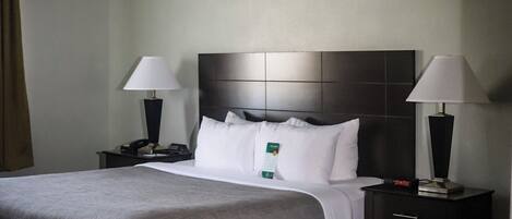 A hotel room with a large bed, two bedside tables with lamps, a headboard, and a nightstand with a phone.