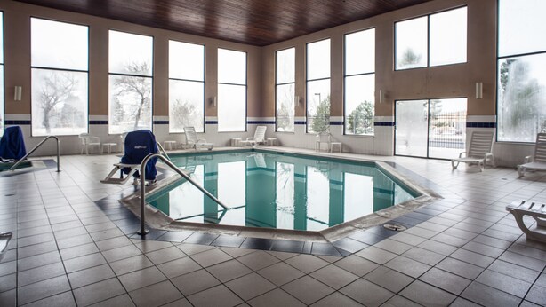 A large indoor swimming pool with clear views through large windows, surrounded by lounge chairs and a tiled floor.