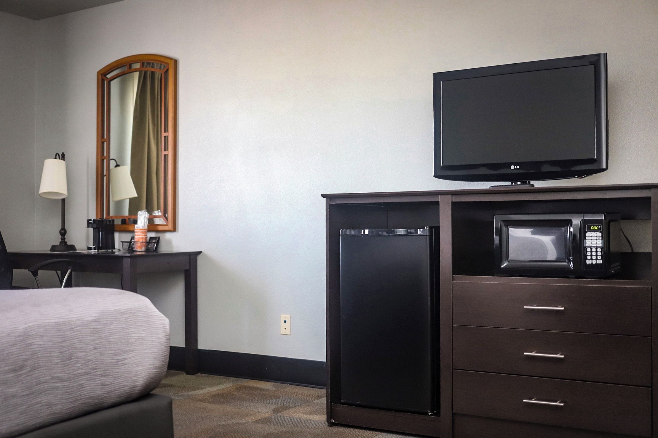A hotel room with a bed, a desk with a lamp, a television, and a microwave.