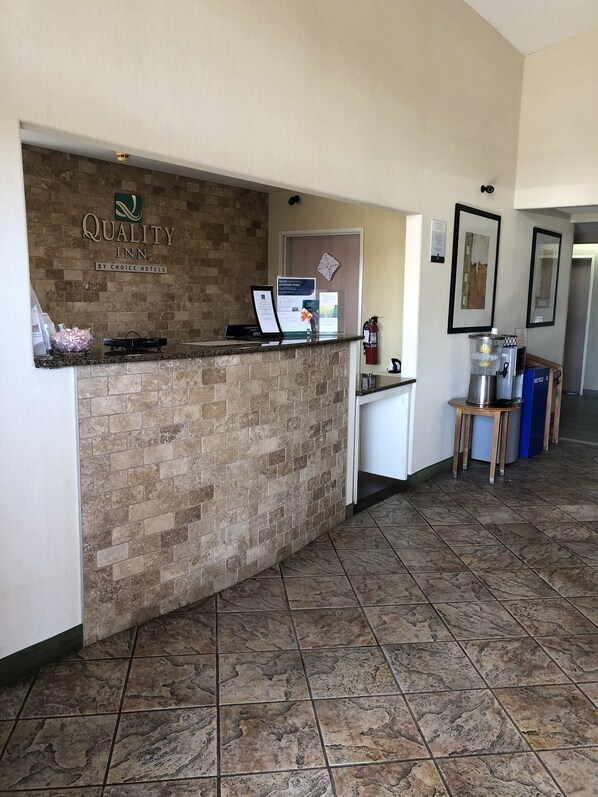 Zona de recepción de un hotel con mostrador de ladrillo, extintor y máquina de café.
