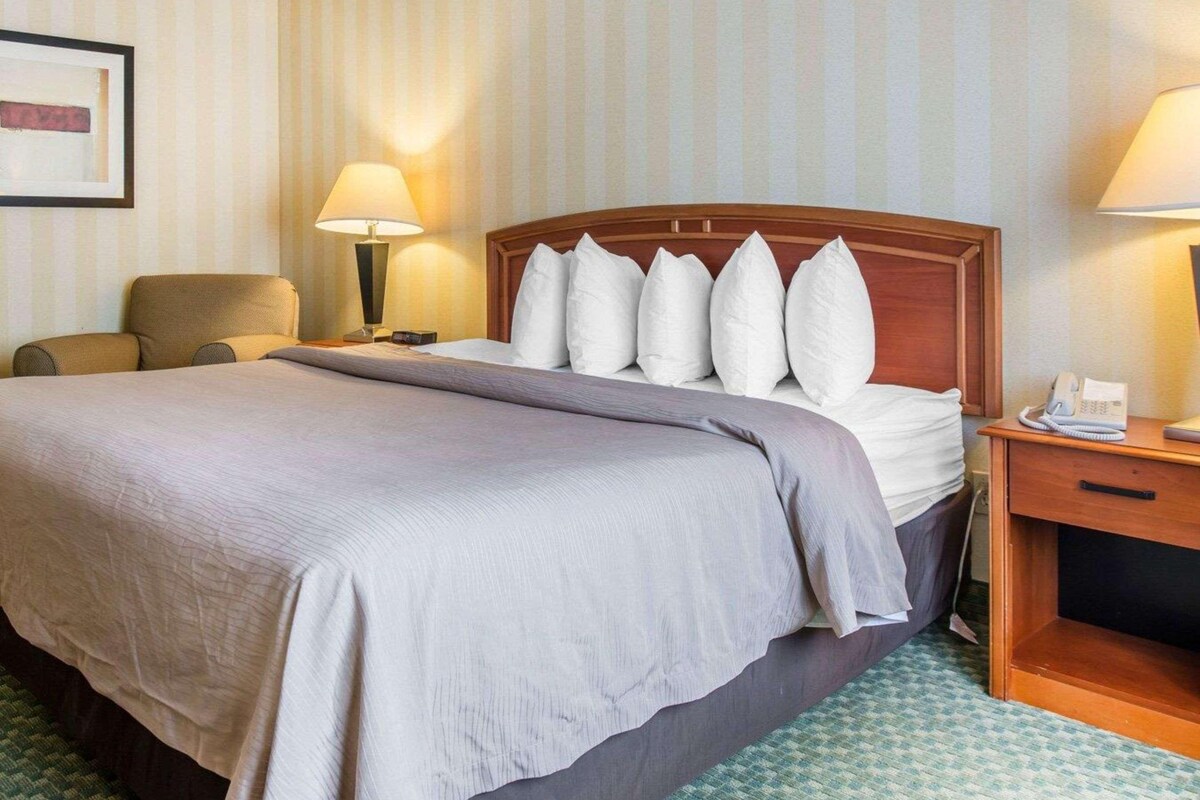 A hotel room with a large bed, two bedside lamps, a wooden nightstand with a phone, and a chair.