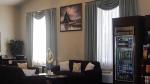 A modern living room with a sofa set, a coffee table, a decorative light fixture, a large window with curtains, and a beverage vending machine.