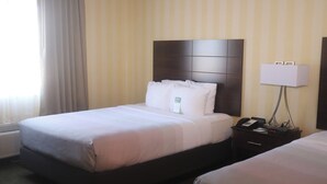 A hotel room with a large bed, a bedside table with a lamp, and a window with curtains.