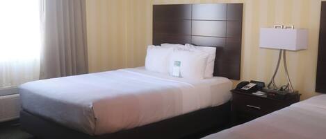 A hotel room with a large bed, a bedside table with a lamp, and a window with curtains.