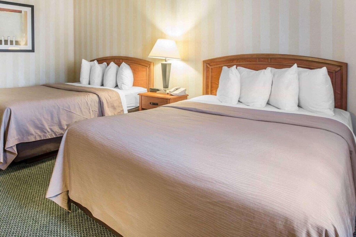 A hotel room with two beds, a nightstand with a lamp, and a striped wall.