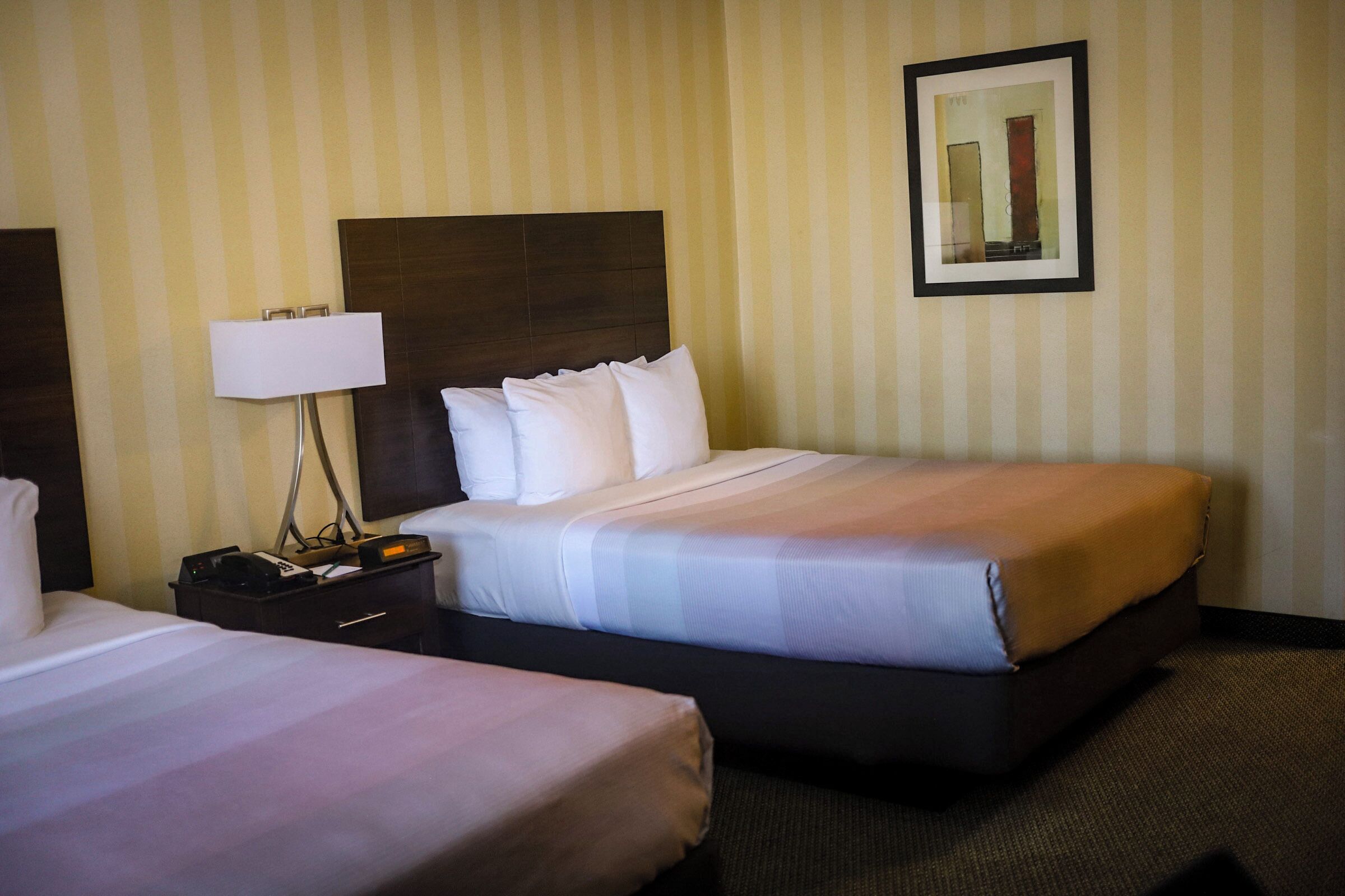 Una habitación de hotel con dos camas, una mesita de noche con lámpara y un cuadro enmarcado en la pared.