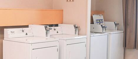 A laundry area with three Whirlpool washers and dryers, a sign for guest laundry, and a bulletin board.