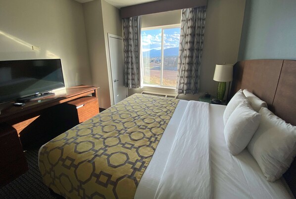 Habitación de hotel con cama, televisión, escritorio y ventana con cortinas.