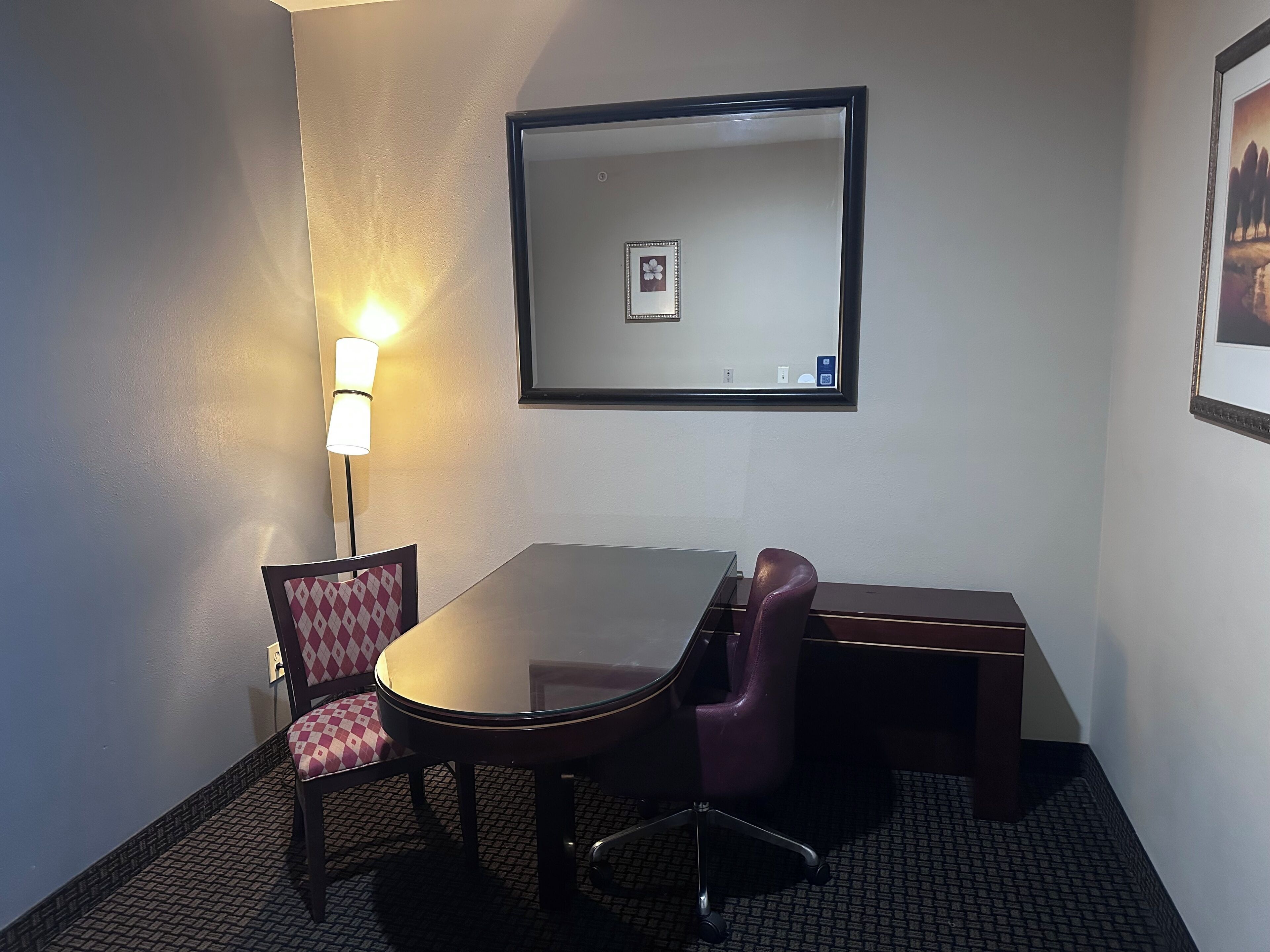 A conference room with a glass table, two chairs, a lamp, and a framed picture on the wall.