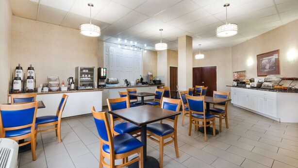 Un comedor limpio y bien iluminado con varias mesas y sillas, una cocina al fondo y una puerta blanca.