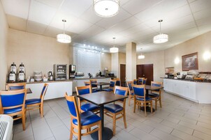 Un comedor limpio y bien iluminado con varias mesas y sillas, una cocina al fondo y una puerta blanca.