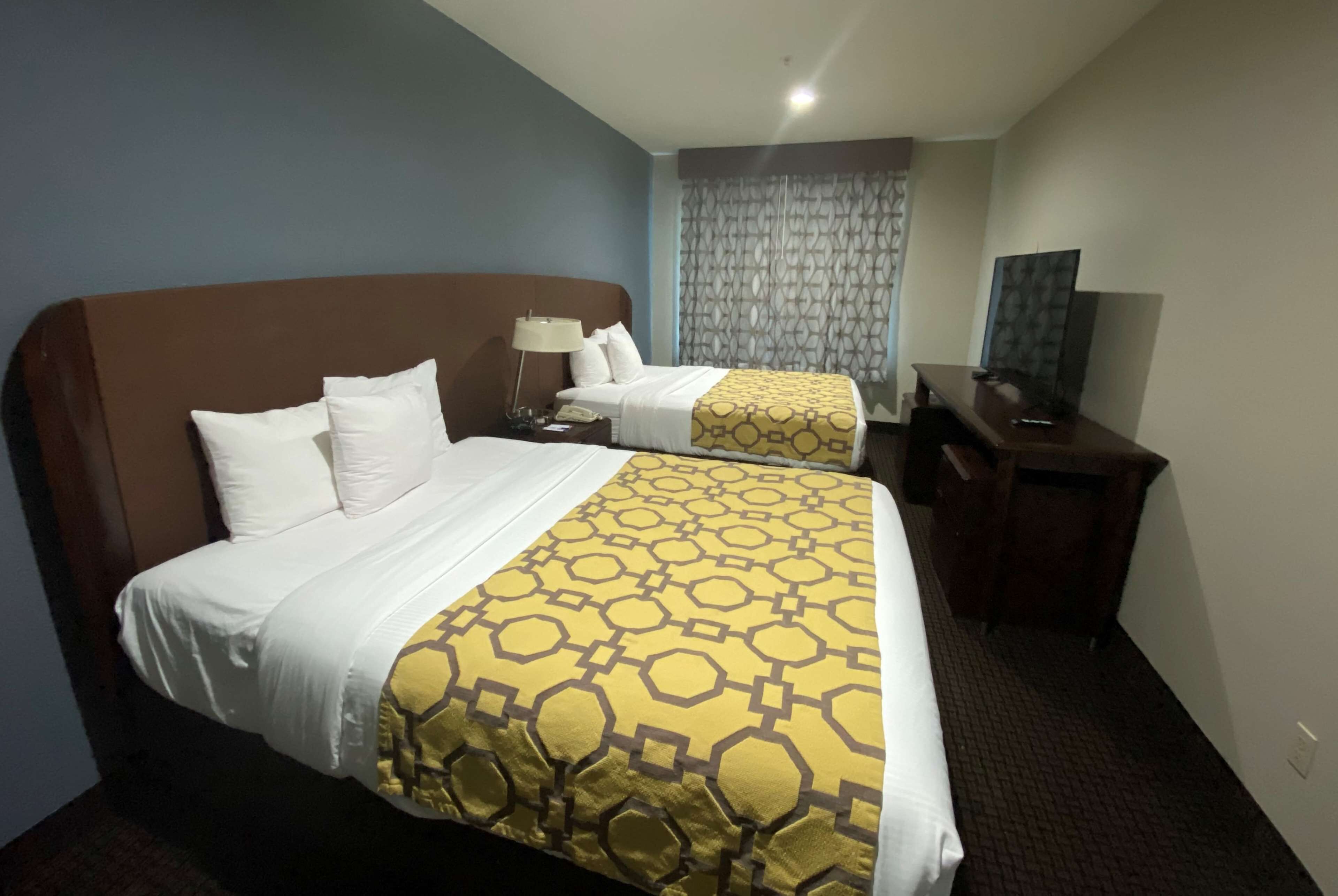 A hotel room with two beds, a desk, and a television.
