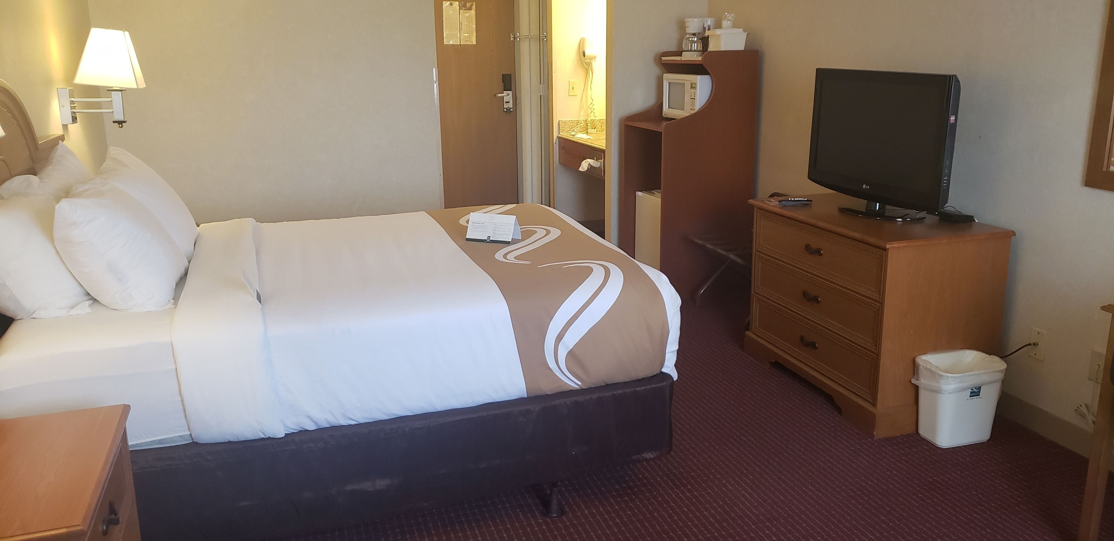 A hotel room with a bed, a television, a desk, and a trash bin.