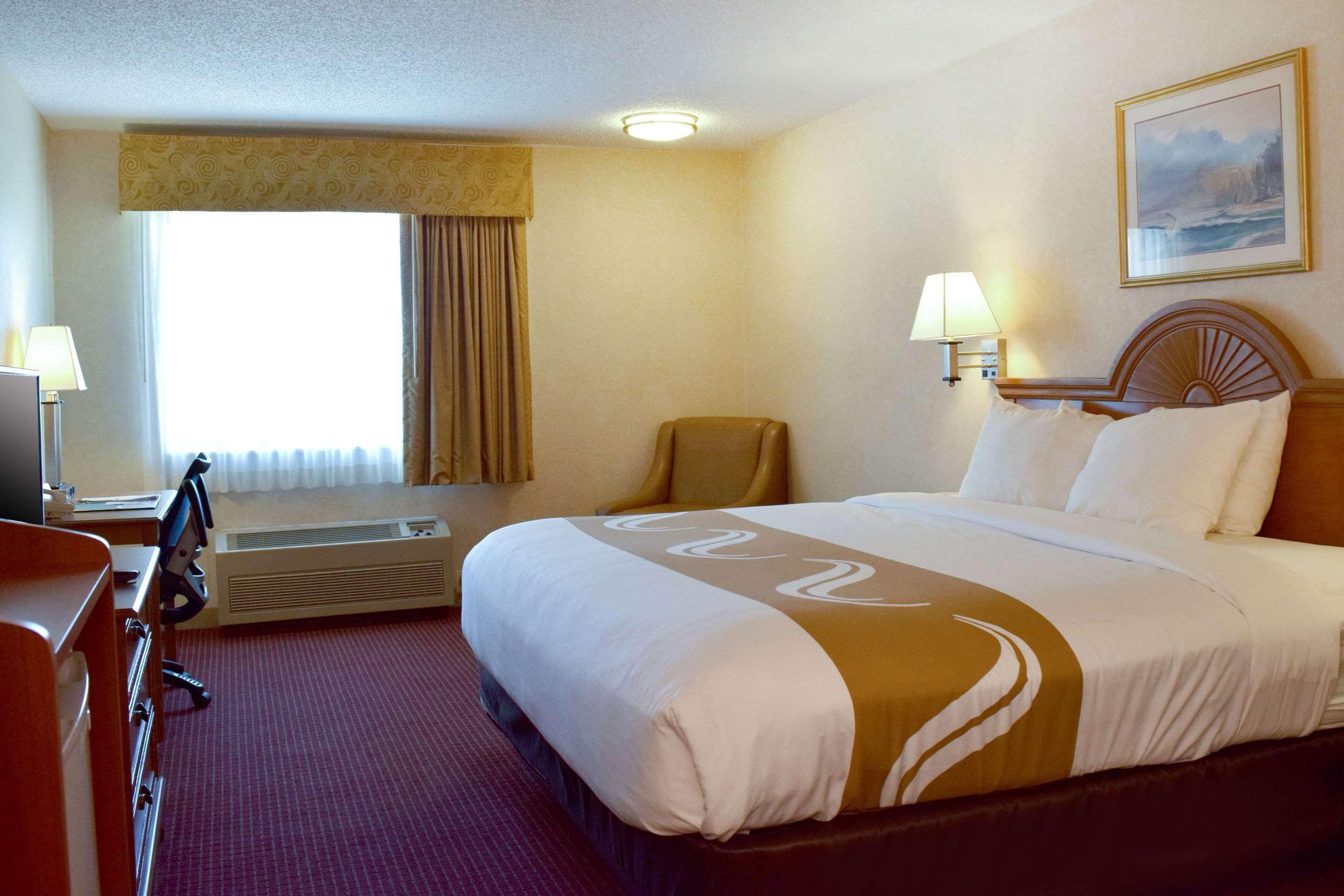 A hotel room with a large bed, a desk, a chair, and a window with curtains.