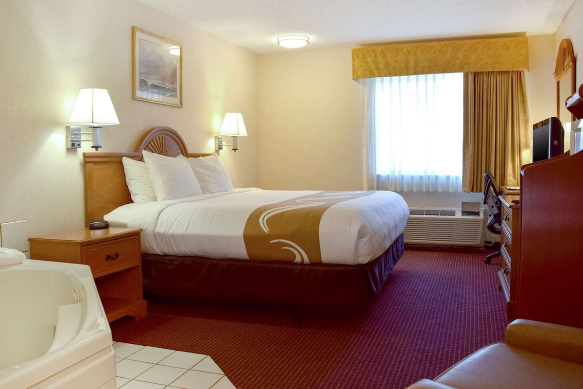 A hotel room with a large bed, two bedside lamps, a TV, a desk, and a chair.