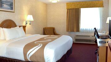 A hotel room with a large bed, a desk with a computer, a chair, a lamp, and a window with curtains.