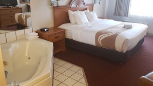 A hotel room with a large bed, a bedside table with a lamp, a chair, a desk, a television, and a bathroom with a bathtub and toilet.