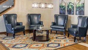 A room with four leather chairs arranged around a glass coffee table, a patterned rug, and abstract art on the wall.