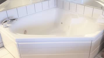 A white freestanding bathtub in a bathroom with white tiled walls and a glass shower enclosure.