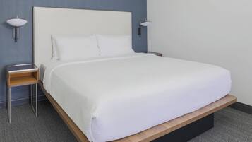 A neatly made bed with white bedding, a wooden platform, and a nightstand with a lamp.