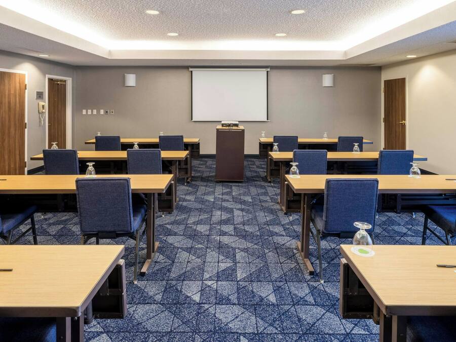 Un salón de conferencias con pantalla de proyector, varias mesas y sillas.
