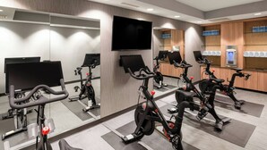 Ein Fitnessraum mit Ergometer, einem Fernseher und einer Trinkstation.
