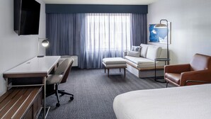 Ein Hotelzimmer mit Bett, Schreibtisch, Stuhl, Sofa und Fernseher.