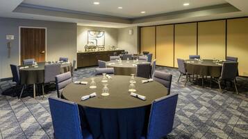 A conference room with multiple tables and chairs, equipped with water glasses and napkins, in a hotel setting.