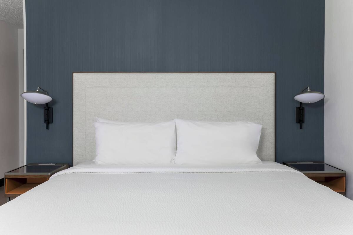 A neatly made bed with white linens, two bedside lamps, and a simple headboard.