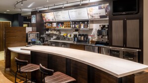 Eine moderne Bar mit einer langen Theke, Barhocker, einer Kaffeemaschine und einer Speisekarte.
