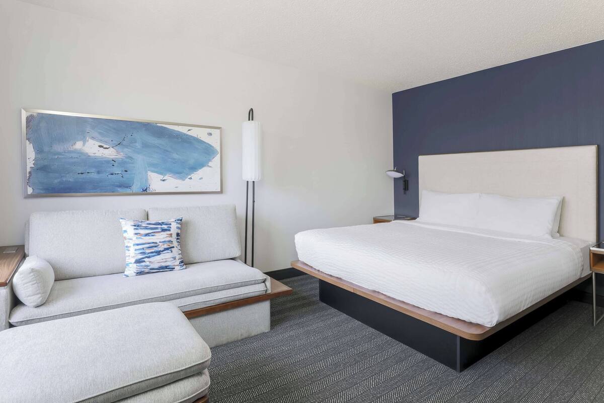 A modern hotel room with a bed, a sofa, a small table, and a floor lamp.