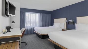 A hotel room with two beds, a desk, a TV, and a window with curtains.