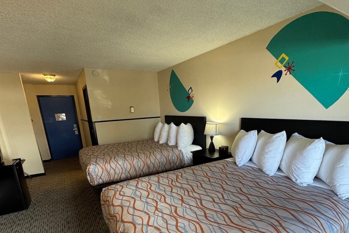 A hotel room with a large bed, a smaller bed, a desk, and a door.