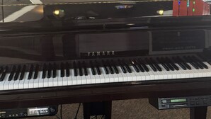 Een Yamaha concertvleugel in een lobby met een receptiebalie, een klok en een plant.
