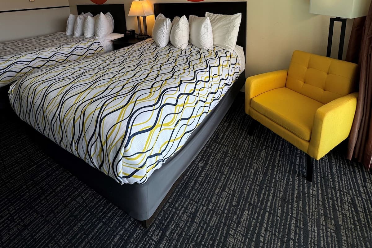 A hotel room with two beds, a yellow armchair, and a red wall decoration.