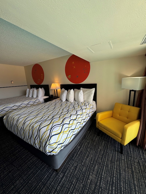 Une chambre d’hôtel avec deux lits, un fauteuil jaune et un élément de décoration rouge sur le mur.