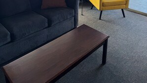 Een kamer met een donkerblauwe bank, een gele fauteuil en een houten salontafel.
