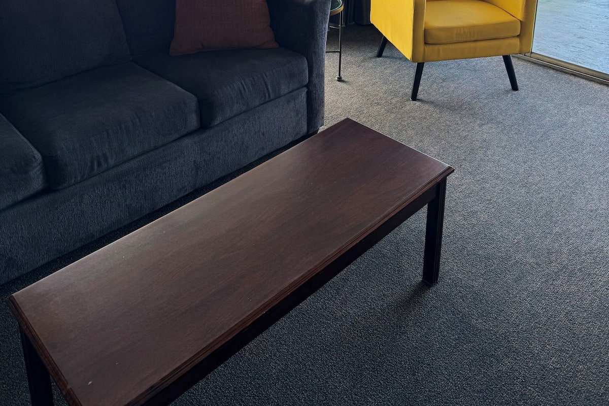 A room with a dark blue sofa, a yellow armchair, and a wooden coffee table.