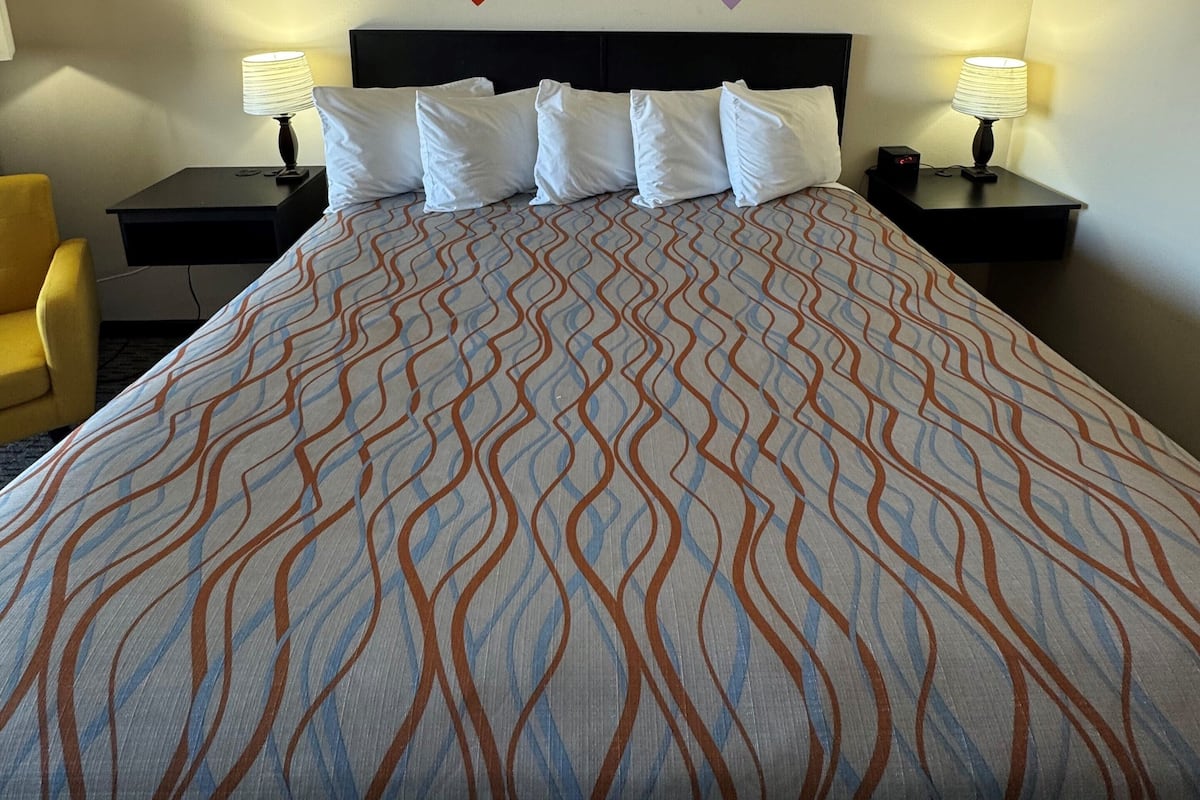A hotel room with a large bed, two bedside tables, a chair, and a wall decoration.