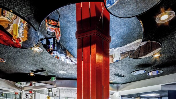 Een lobby met een centrale rode en blauwe pilaar, een rond zitgedeelte en een glazen tafel die het interieur van de ruimte weerspiegelt.