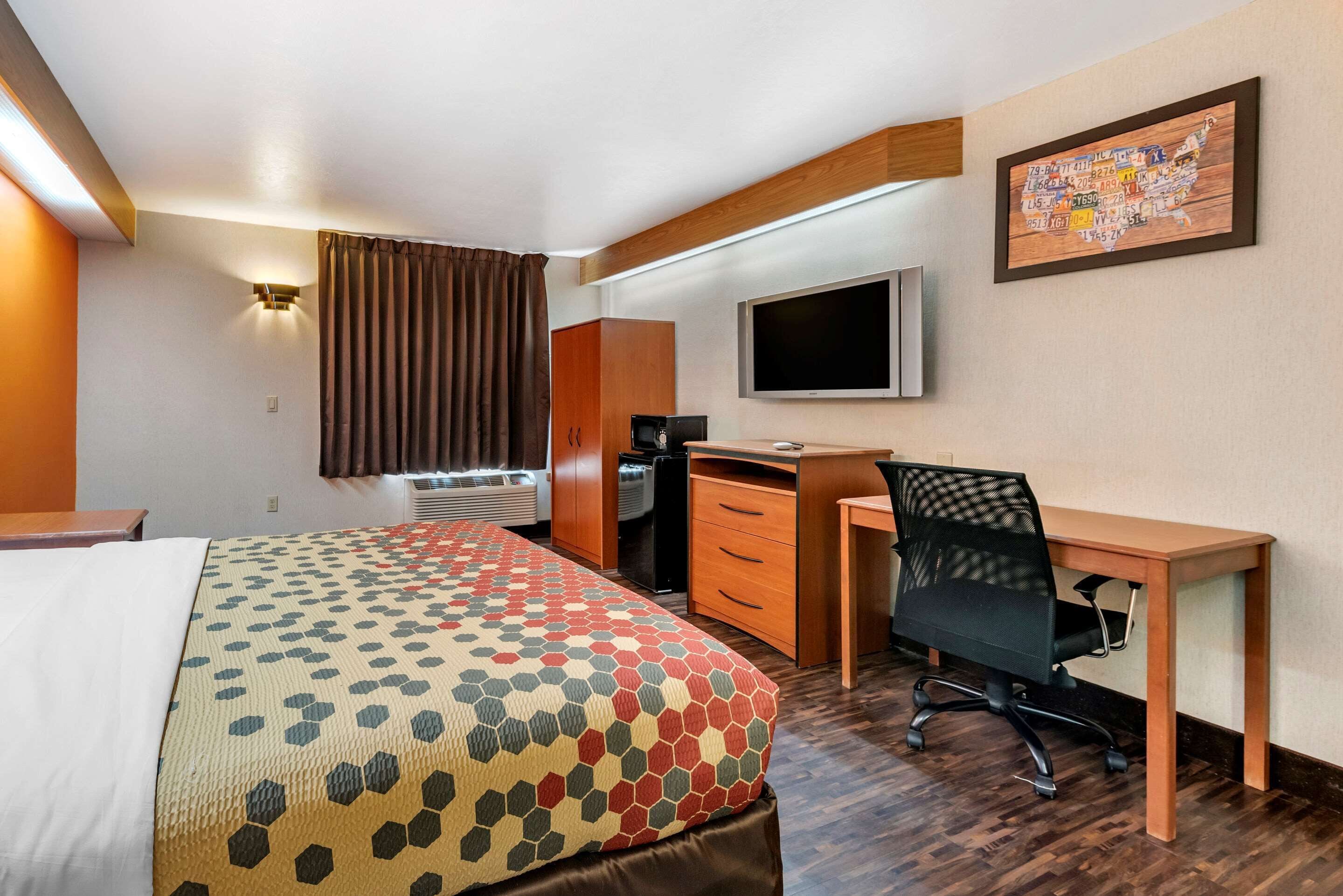 A hotel room with a bed, a desk, a chair, a television, and a coffee machine.