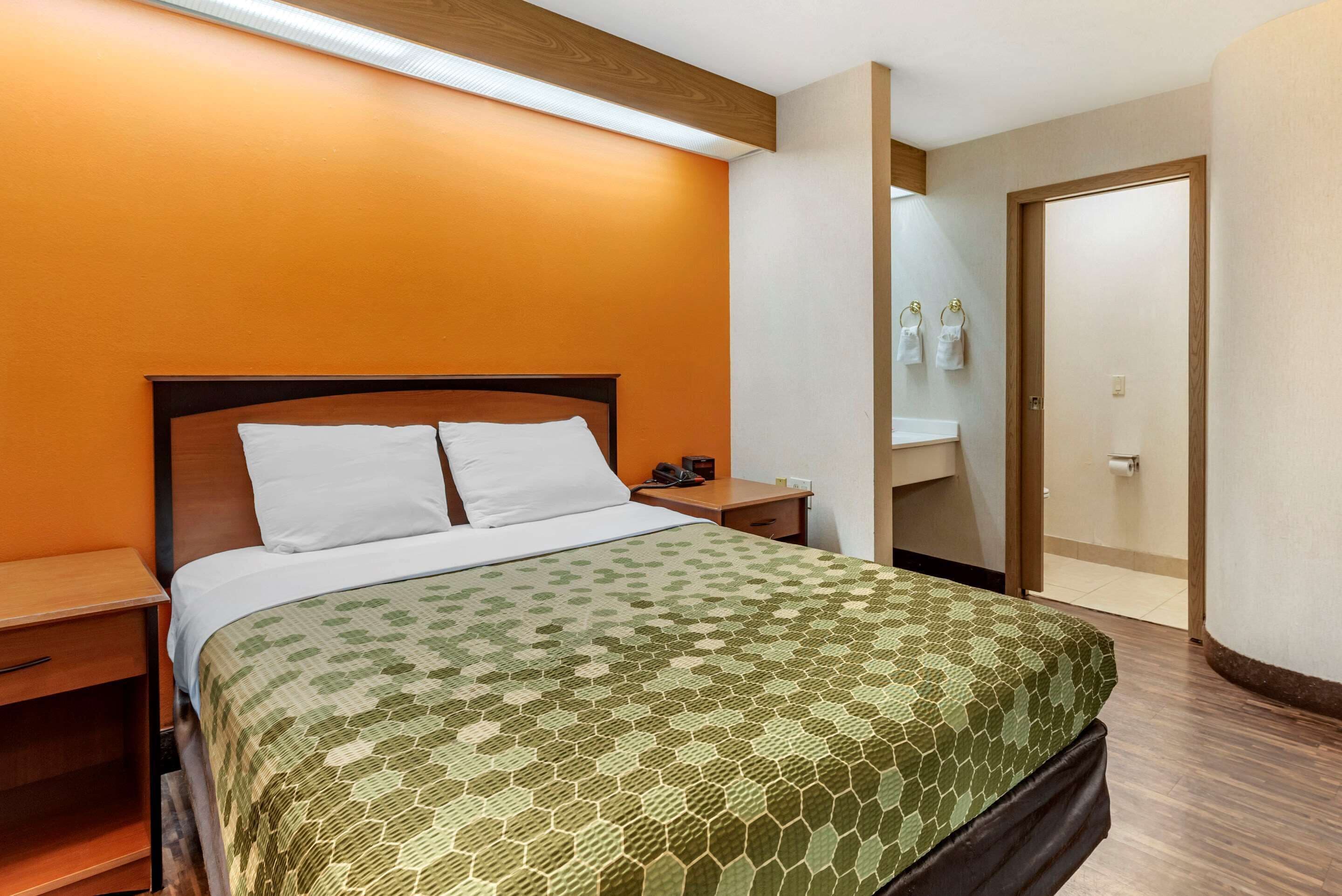 A hotel room with a bed, a nightstand, a bedside table, a bathroom with a sink and mirror, and a door.