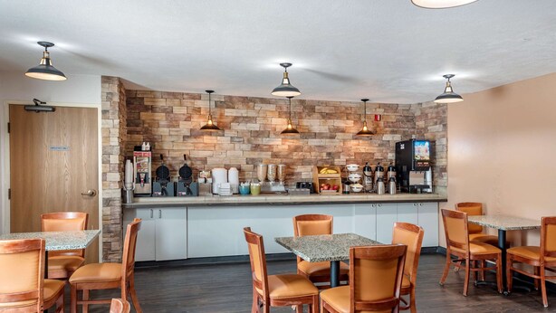 A restaurant with a stone wall backdrop, multiple tables and chairs, and a coffee bar with various appliances. - Econo Lodge North Academy (Colorado Springs)
