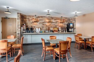 Un restaurante con un fondo de pared de piedra, varias mesas y sillas, y una barra de café con diversos equipos.